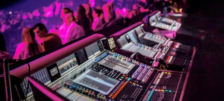 Professionele digitale mengtafels in de FOH-regieruimte tijdens een live concert met publiek.